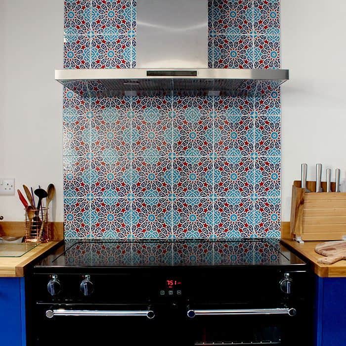 Kitchen with colorful patterned tile backsplash behind stove, stainless hood, and wooden countertops with utensils.