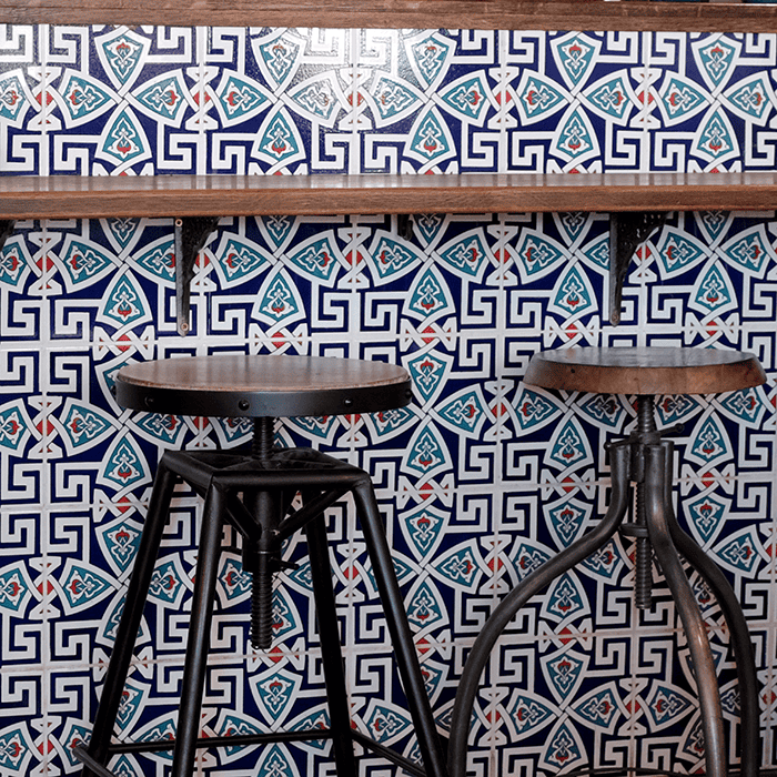 Bar seating area with blue geometric patterned tile wall, wooden counter, and industrial-style metal stools.