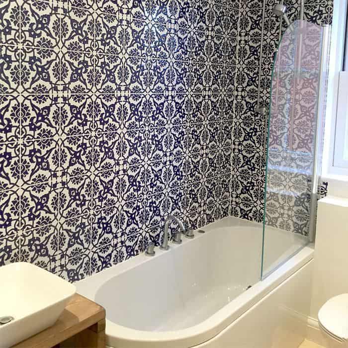 Bathtub with glass shower screen against a wall of intricate blue and white patterned tiles in a modern bathroom.