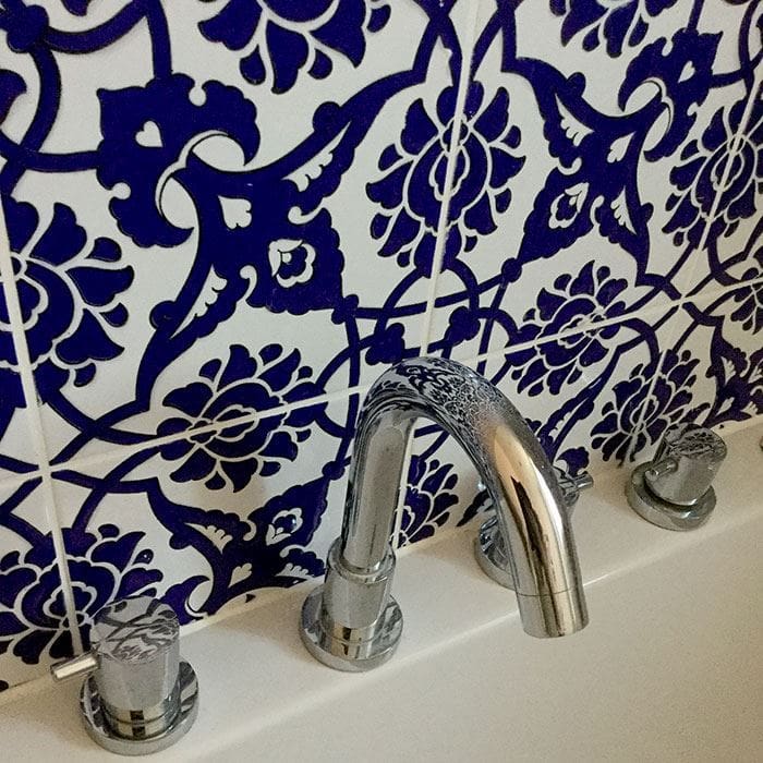 Chrome bathtub faucet and handles against bold blue and white floral patterned tile wall.