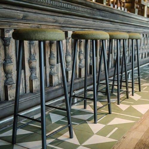 Square ceramic tiles in muted green and off-white, with varied geometric shapes, forming a cohesive modern decorative interior pattern.