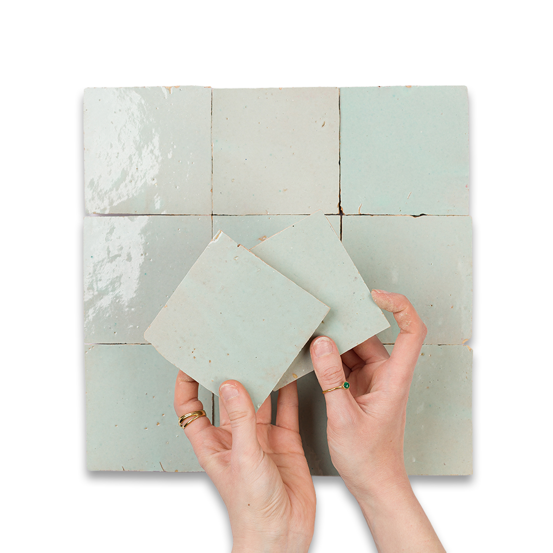 Hands holding a small square tile against a larger grid of tiles on a white background