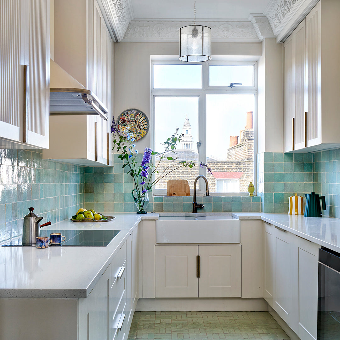 Modern kitchen with white cabinets, green tiled backsplash, and a window view.