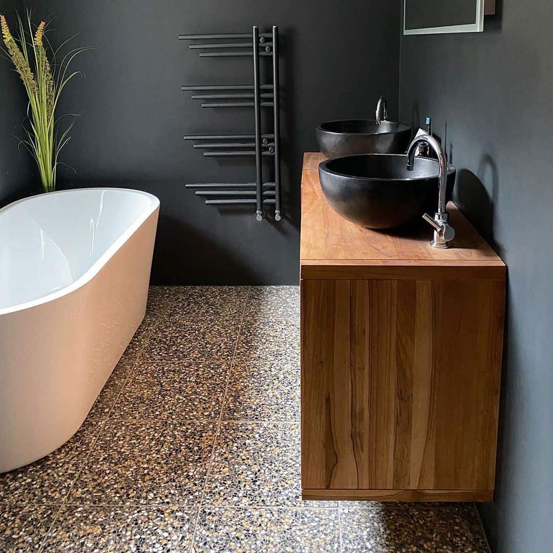 Modern bathroom with terrazzo flooring, freestanding tub, wooden vanity, and dual black vessel sinks.