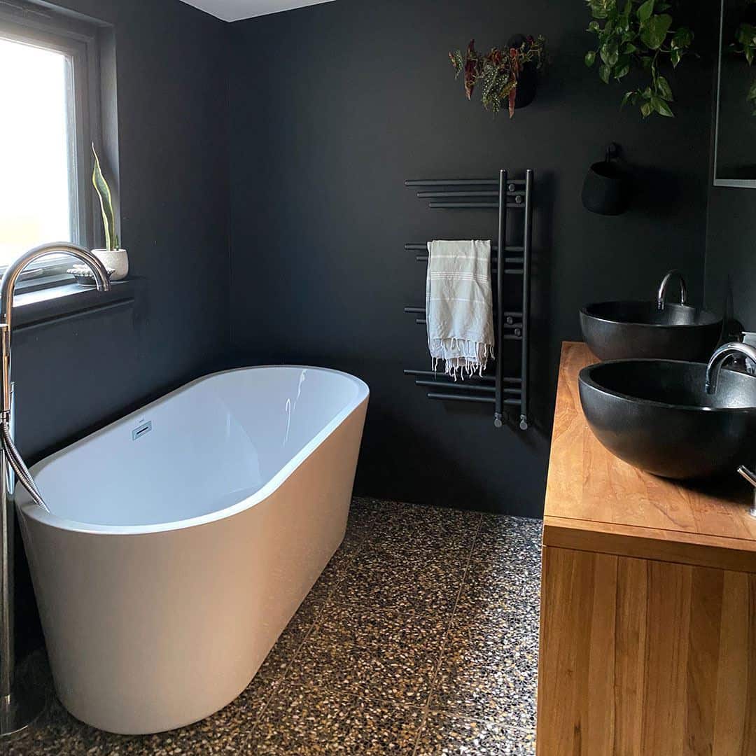 Modern bathroom with terrazzo flooring, freestanding tub, wooden vanity, and dual black vessel sinks.