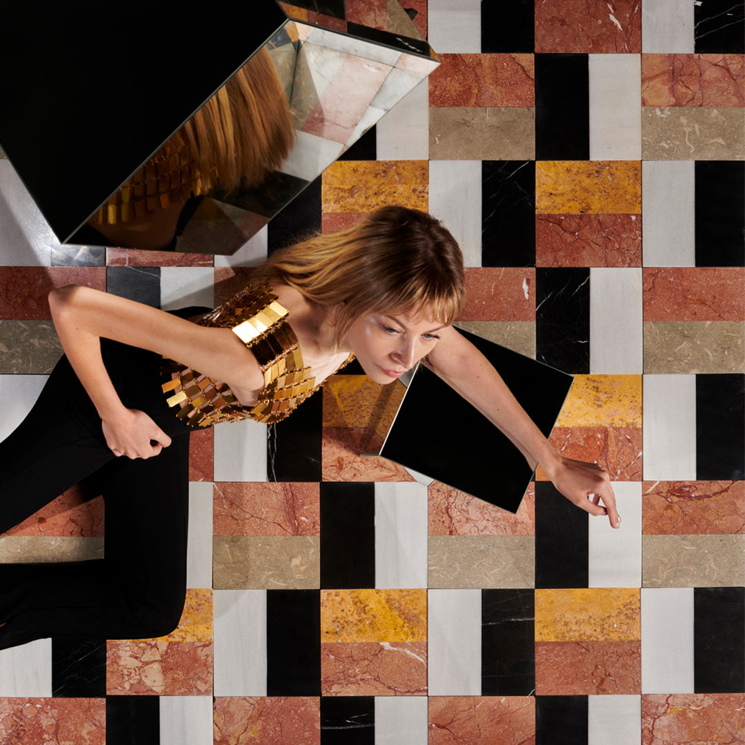 Woman in a gold dress sitting on a checkered floor with abstract patterns