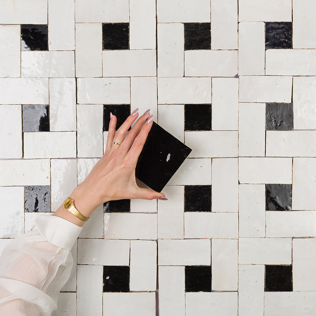Hand holding a black square against a tiled wall with a geometric pattern