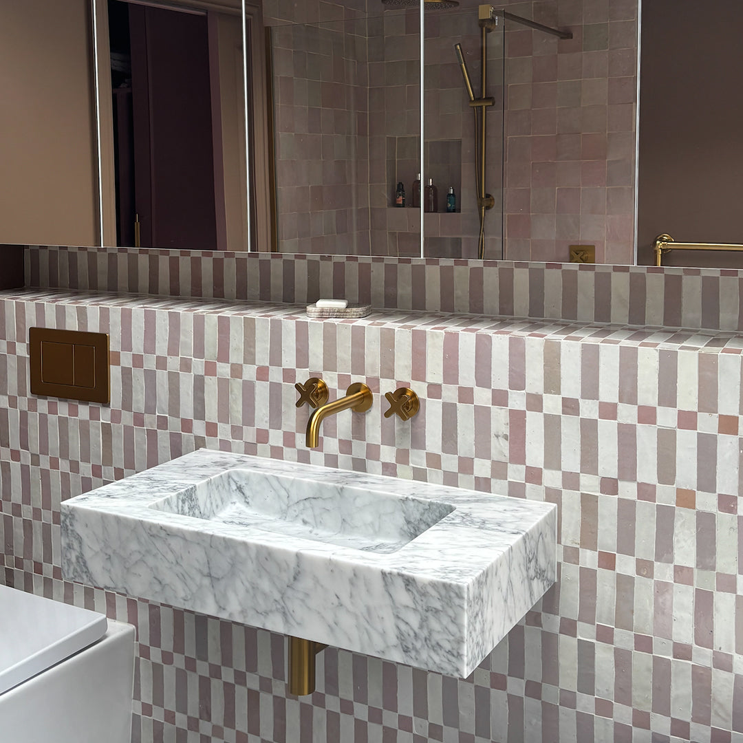 Bathroom with marble sink and gold fixtures against a patterned wall.