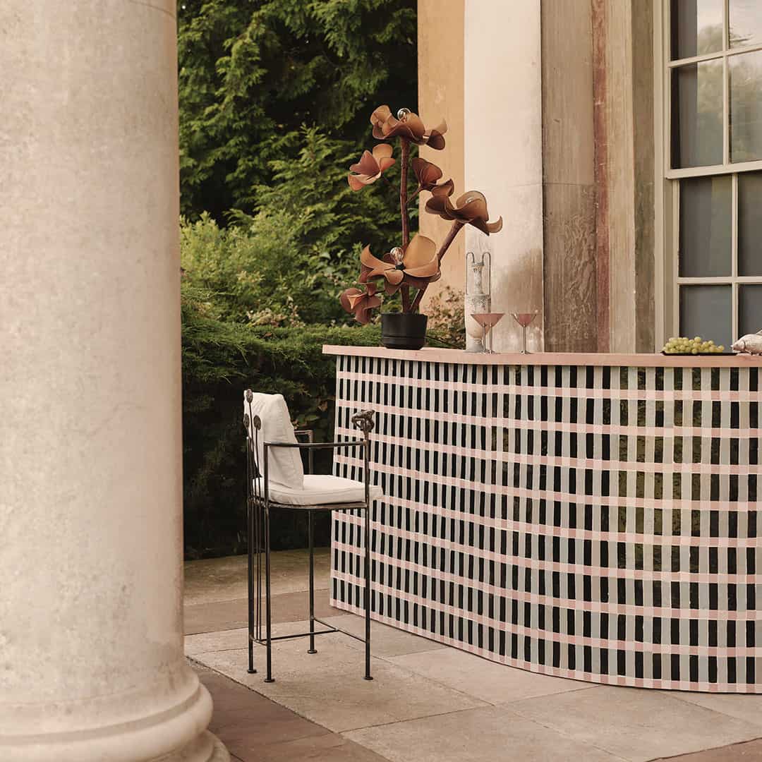 Outdoor bar with striped counter, martini glasses, plant decor, and lush garden backdrop.