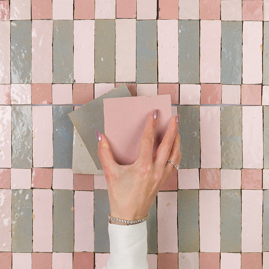 Hand holding a pink tile against a mosaic tile wall
