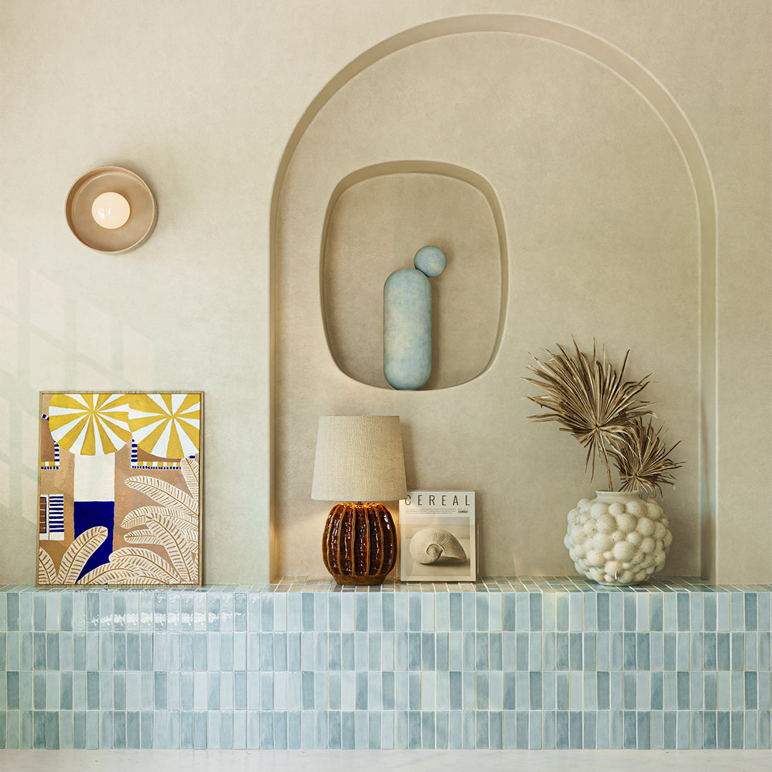 Decorative shelf with a lamp, vase, and abstract art piece against a beige wall.