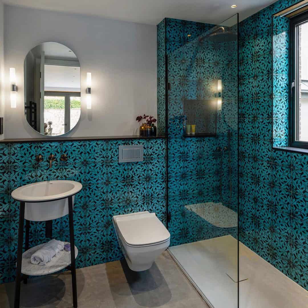 Contemporary bathroom with turquoise patterned tiles, wall-mounted toilet, round sink, and glass-enclosed shower.