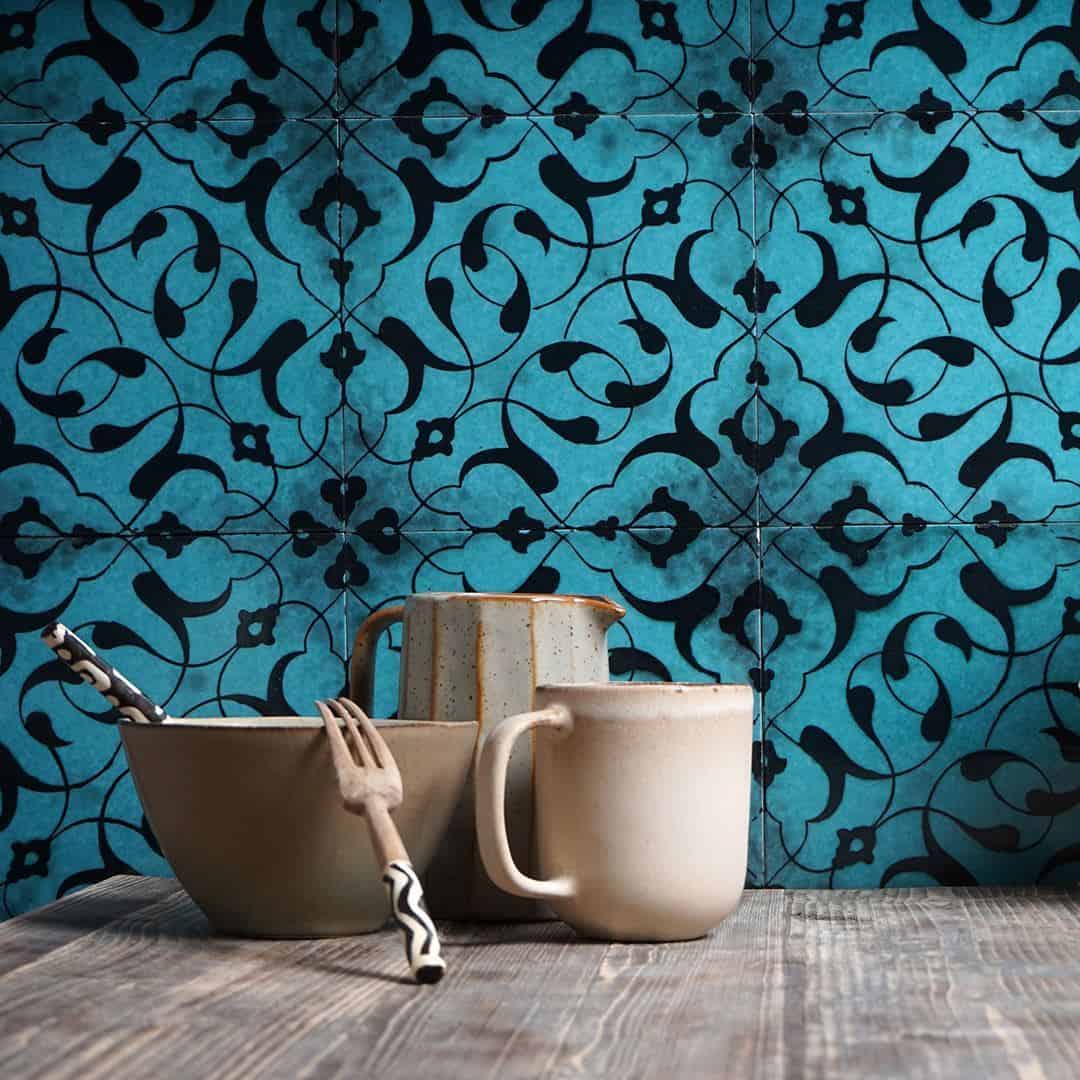 Still life with beige ceramics, patterned utensils, and blue floral tile background.
