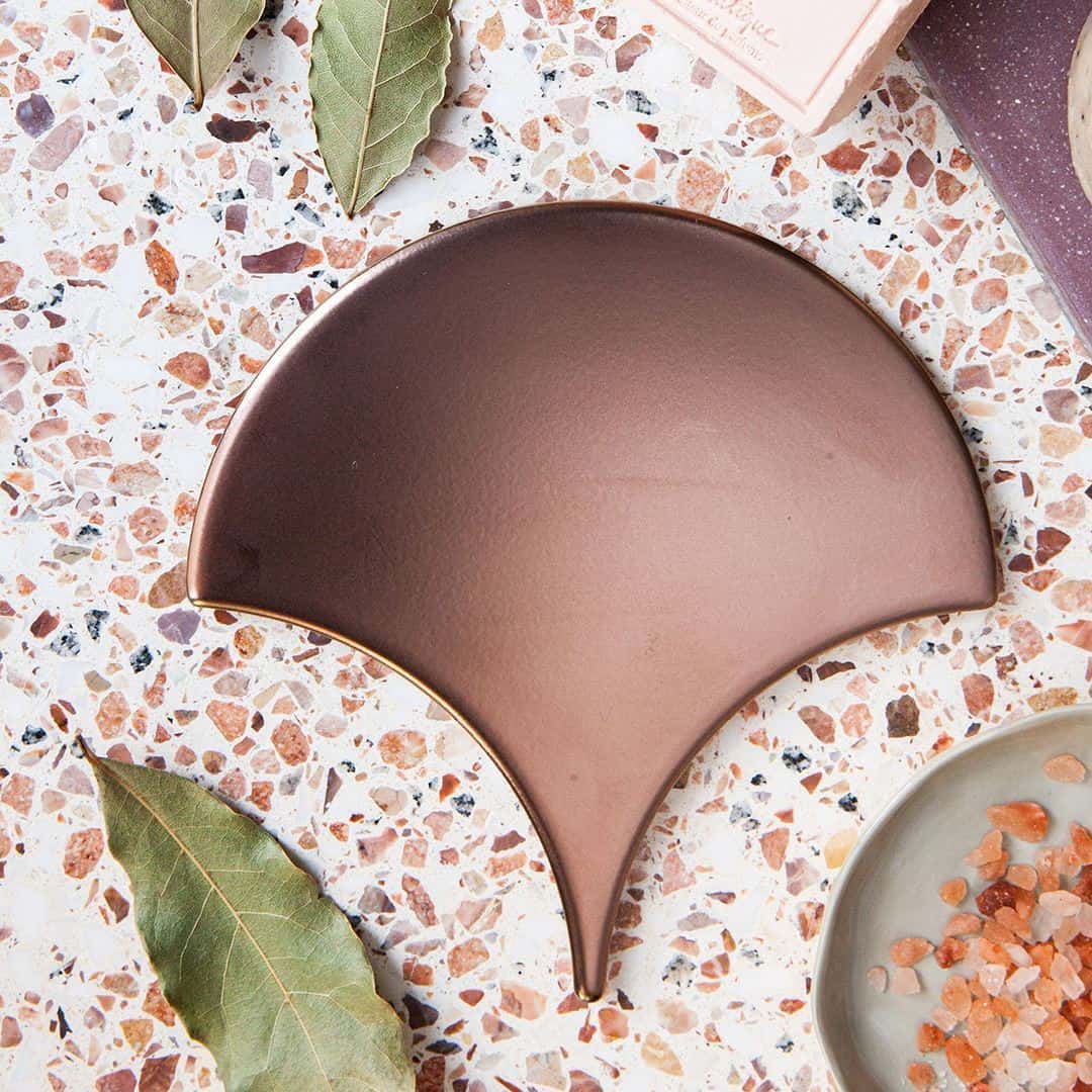 Decorative ceramic tray on terrazzo surface with bay leaves and pink salt, styled in warm earthy tones.