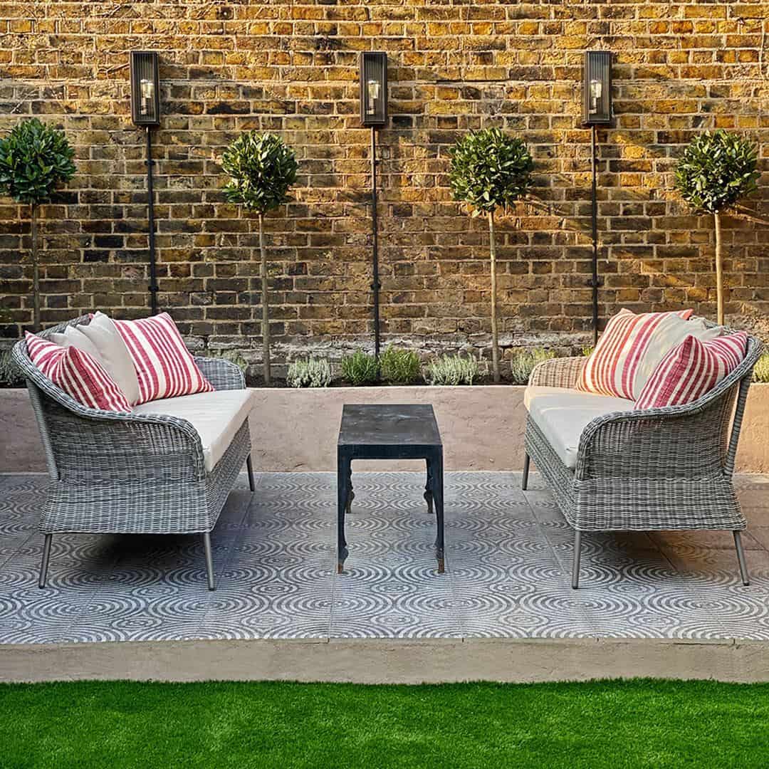 A square cement tile featuring a textured gray surface with concentric circular patterns intersecting at the center, creating a geometric, symmetrical, and modern decorative design.