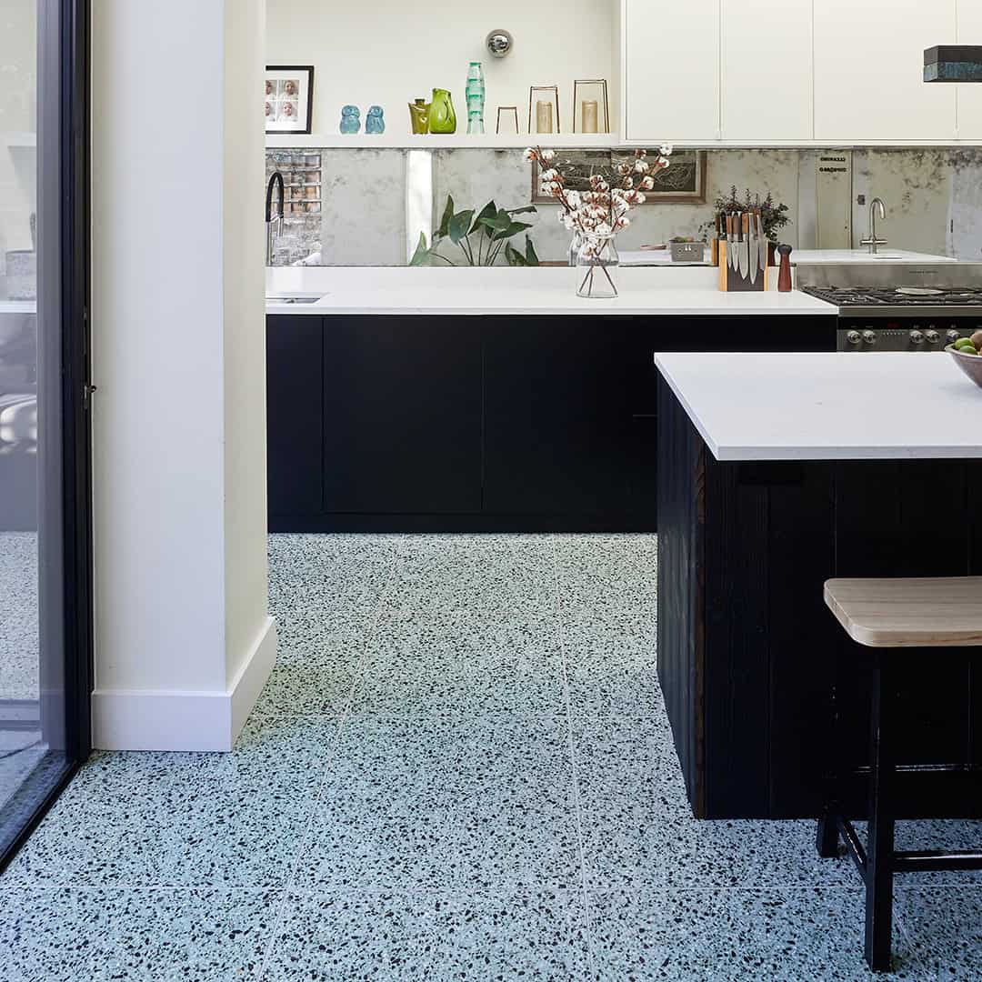Modern kitchen with terrazzo flooring, black cabinetry, white countertops, and minimalist decor accents.