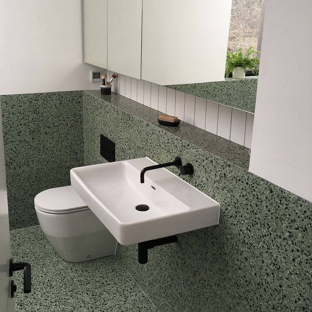 Minimalist bathroom with green terrazzo walls and floor, white wall-mounted sink, and matte black fixtures.