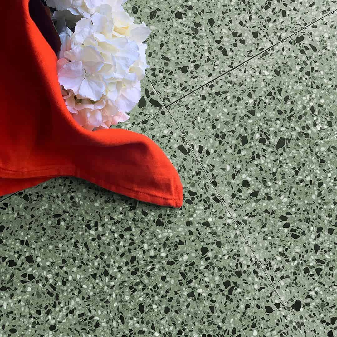 Green terrazzo tile floor with white flowers and red fabric creating a bold color contrast.