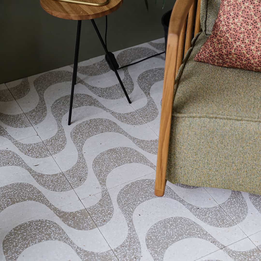 A square cement tile featuring a white background with curved beige wave-like patterns filled with small white speckles, creating a soft, organic, and modern decorative design.