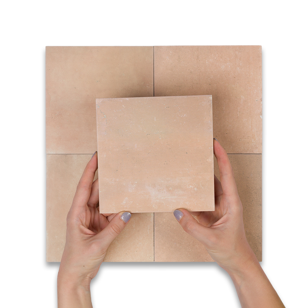 Hands holding a square piece of brown paper against a tiled cardboard background