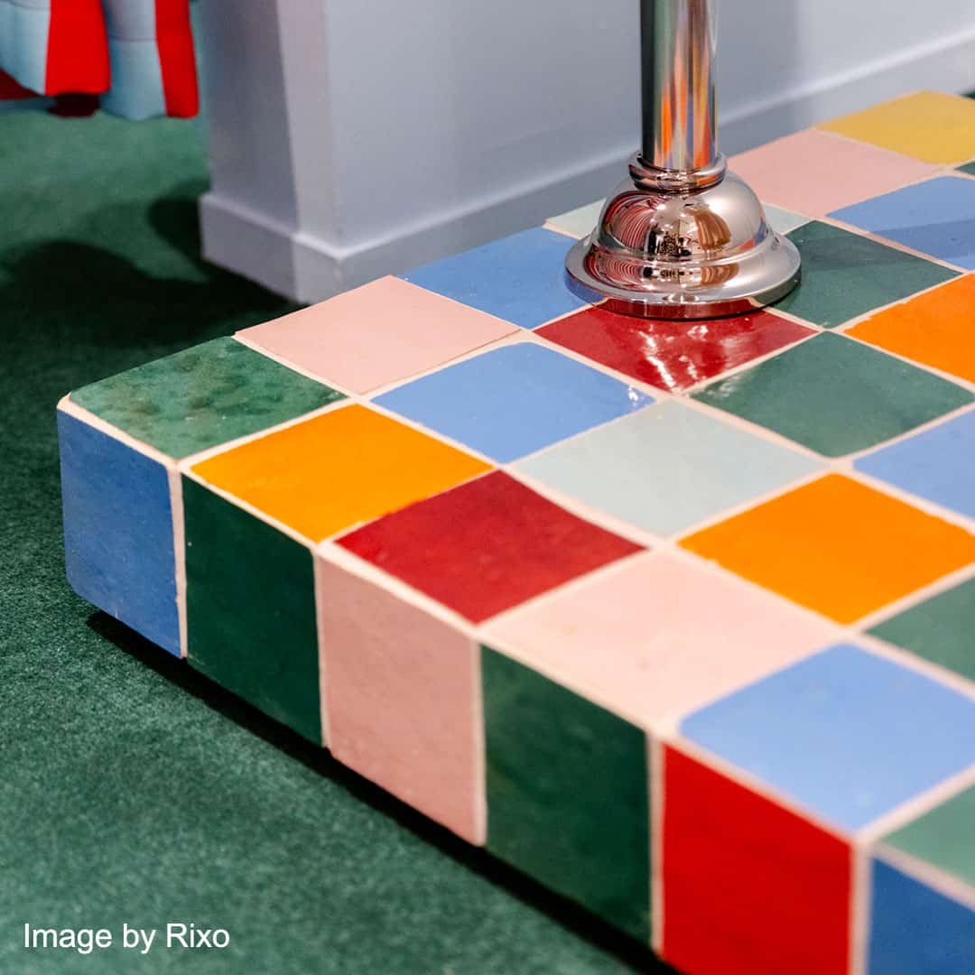 Colorful checkerboard tiled platform with chrome pole, green carpet, and gray wall background.