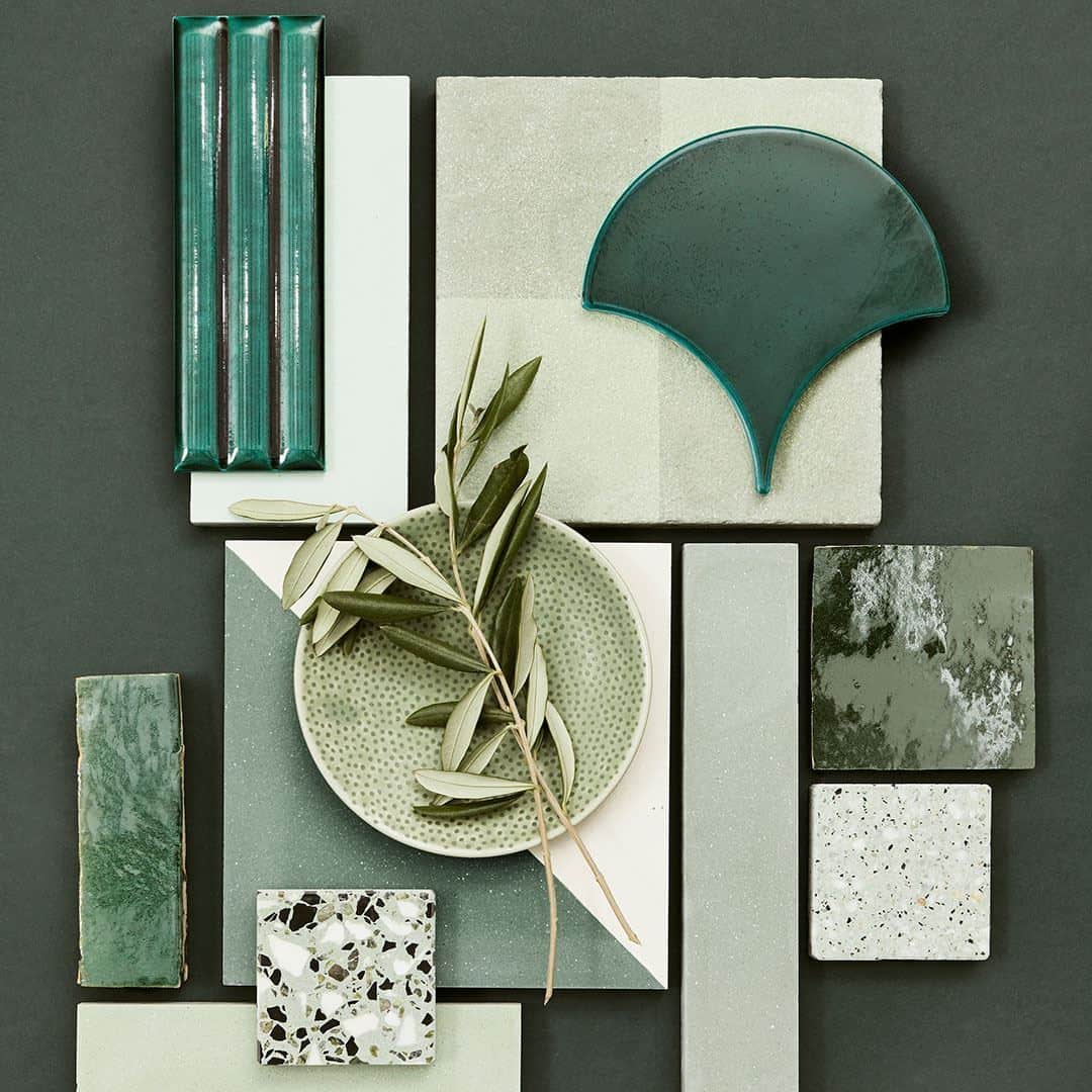 Flat lay of green-toned tile samples, terrazzo pieces, ceramic shapes, and olive branch on a dark background.