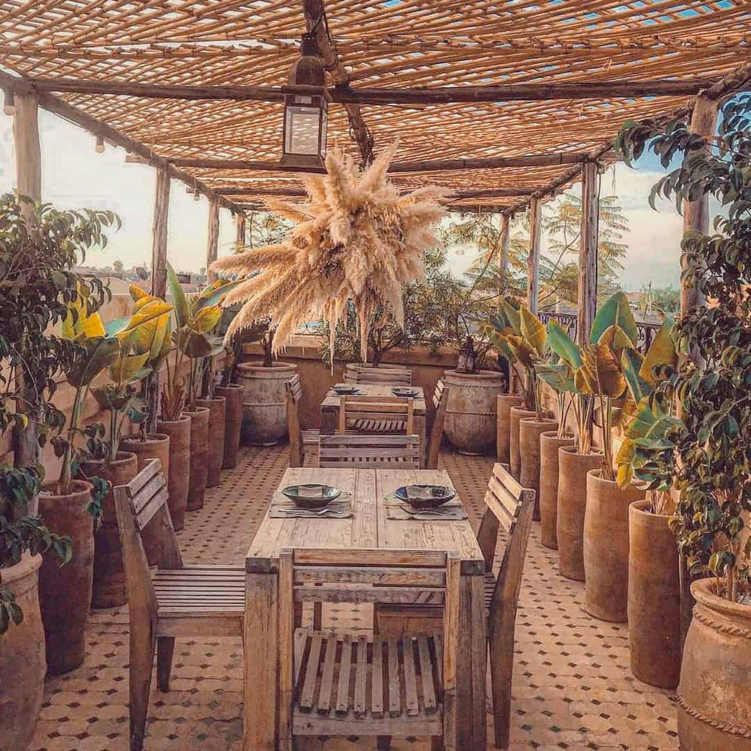 Cozy rooftop dining area with wooden furniture, geometric tiles, and hanging pampas grass.