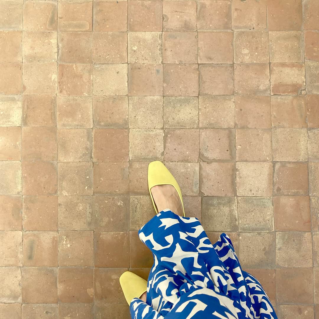 Top-down view of a person standing on a terracotta-tiled floor. The tiles are square and arranged in a grid pattern. 
