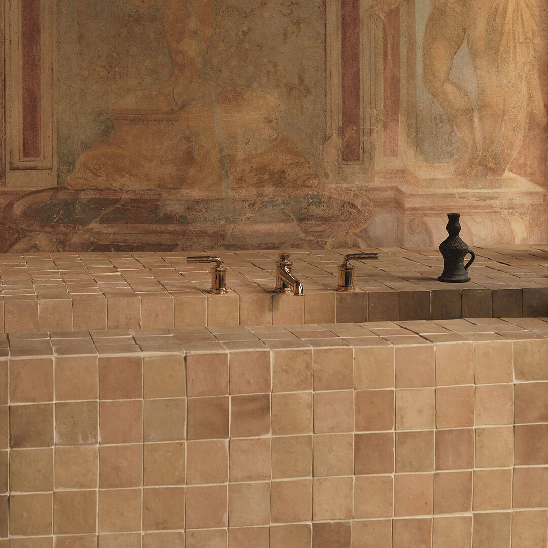 A tiled sink area with square beige tiles and three metallic faucets along the top edge. 