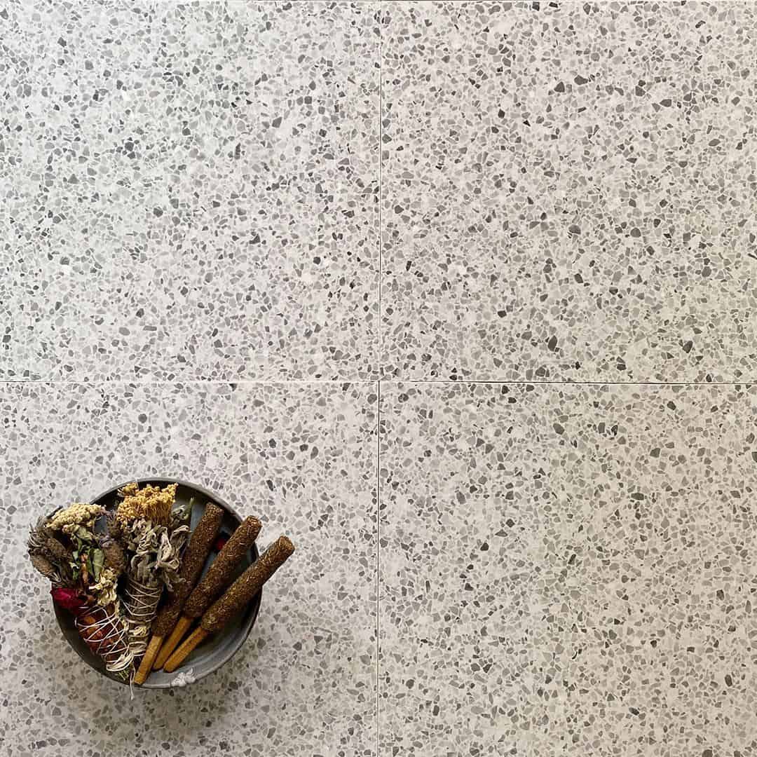 Light terrazzo tile floor with subtle gray stone chips, styled with a small bowl of dried herbs and incense sticks.