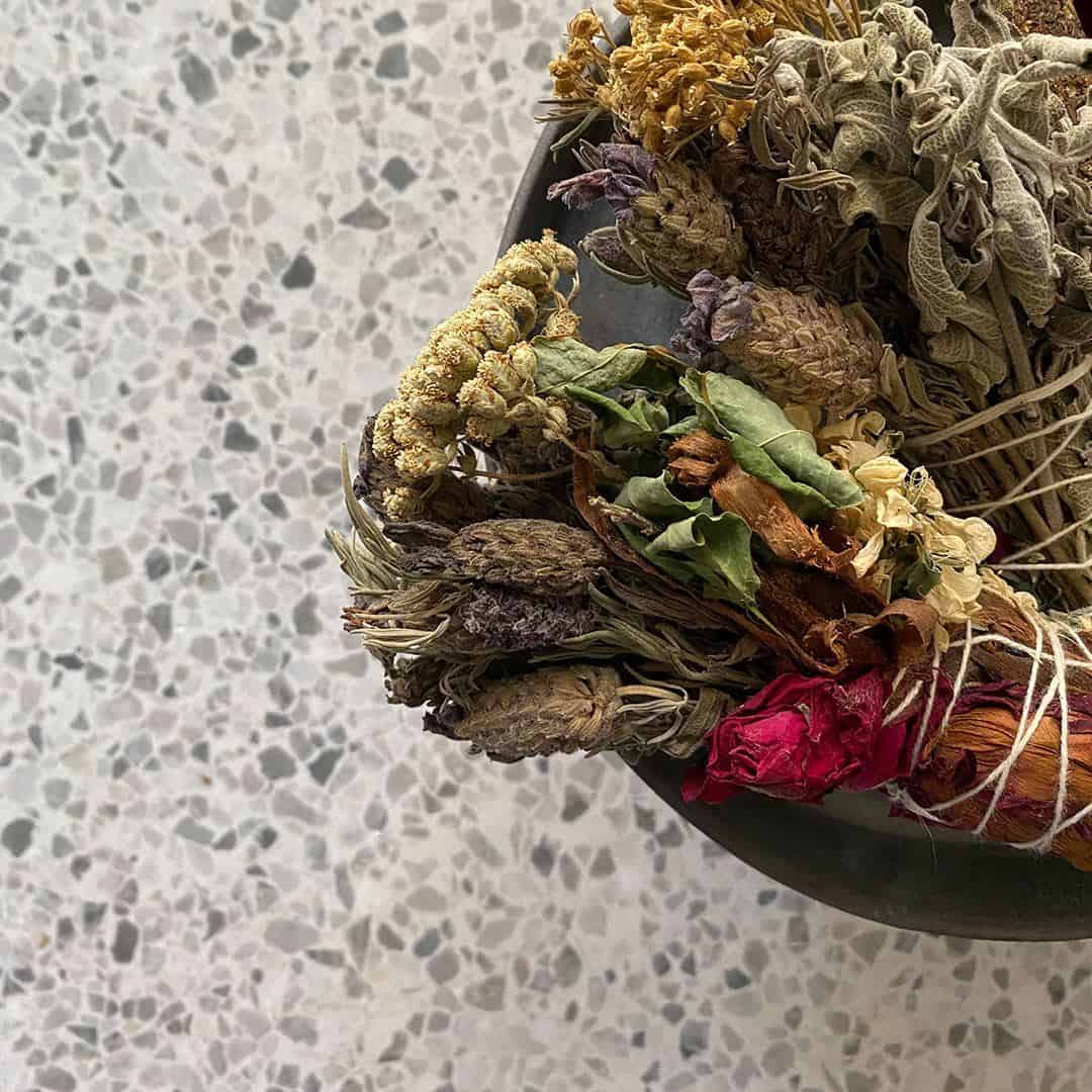 Light terrazzo tile floor with subtle gray stone chips, styled with a bowl of dried herbs.