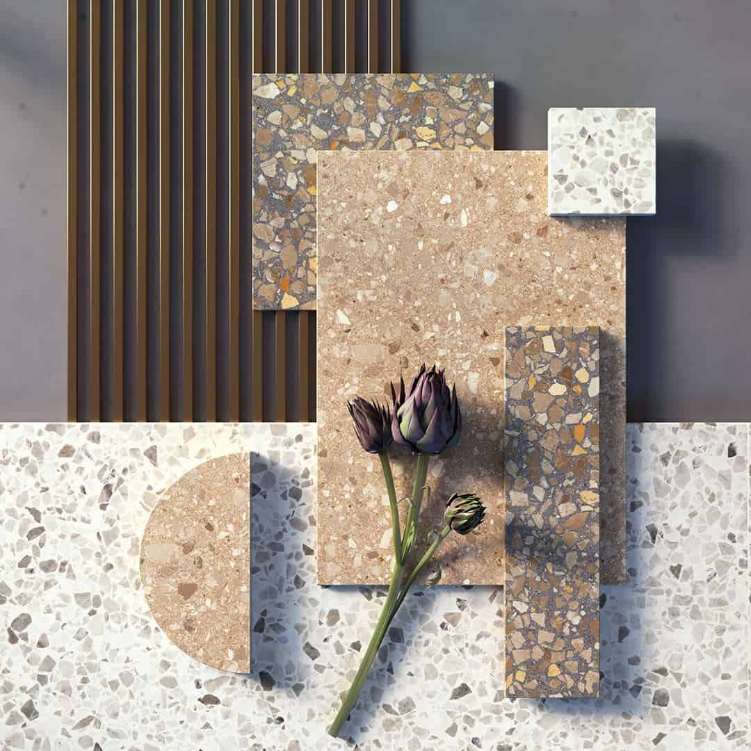 Assorted terrazzo tile samples in neutral tones arranged with a flower and wood panel backdrop in a styled composition.