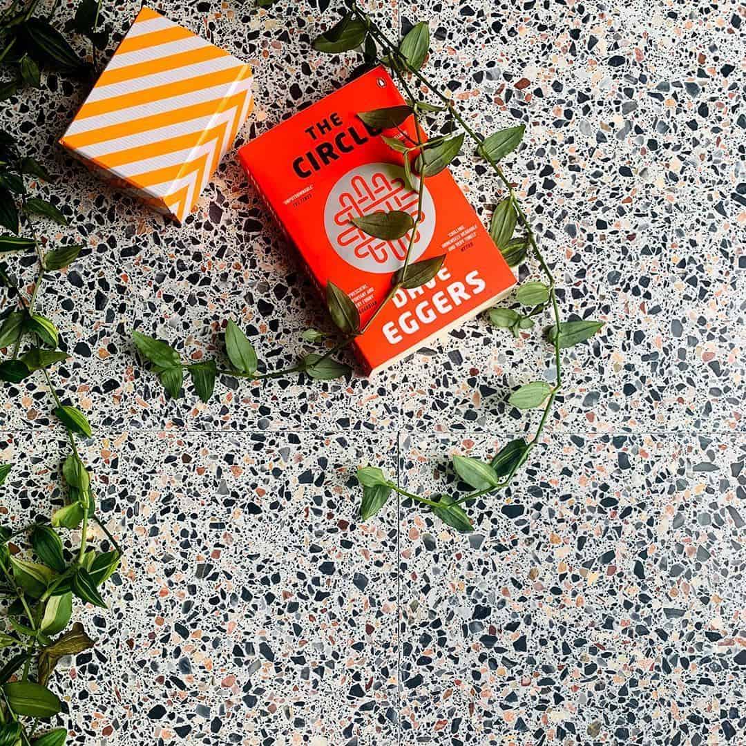 Multicolor terrazzo tile floor with book, striped box, and green vine styled decor.