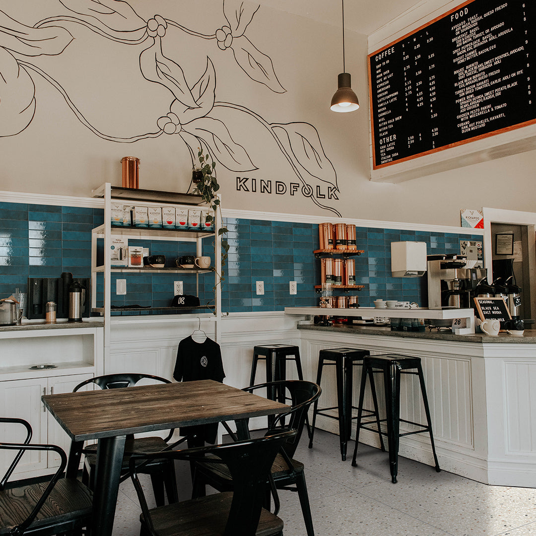 Interior of a coffee shop named 'Kindfolk' with tables, chairs, and a menu board.