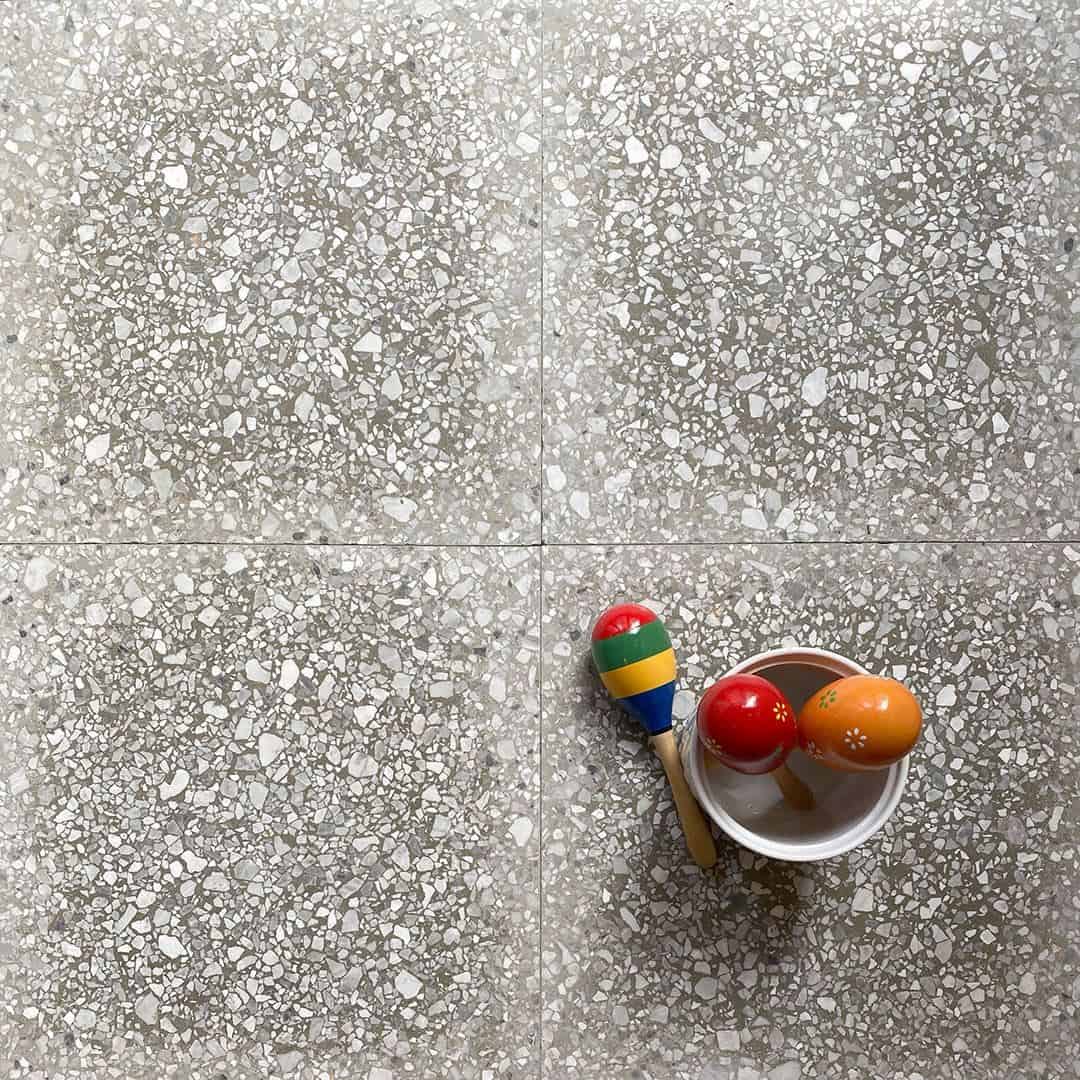Neutral terrazzo tile floor with fine stone chips, styled with colorful wooden maracas in a small bowl.