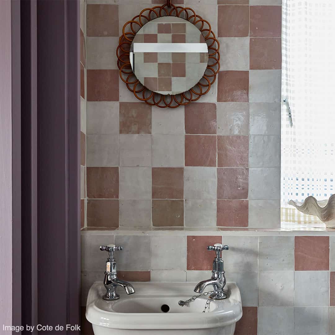  Small bathroom sink with chrome faucets set against a wall of pink and beige square tiles. 
