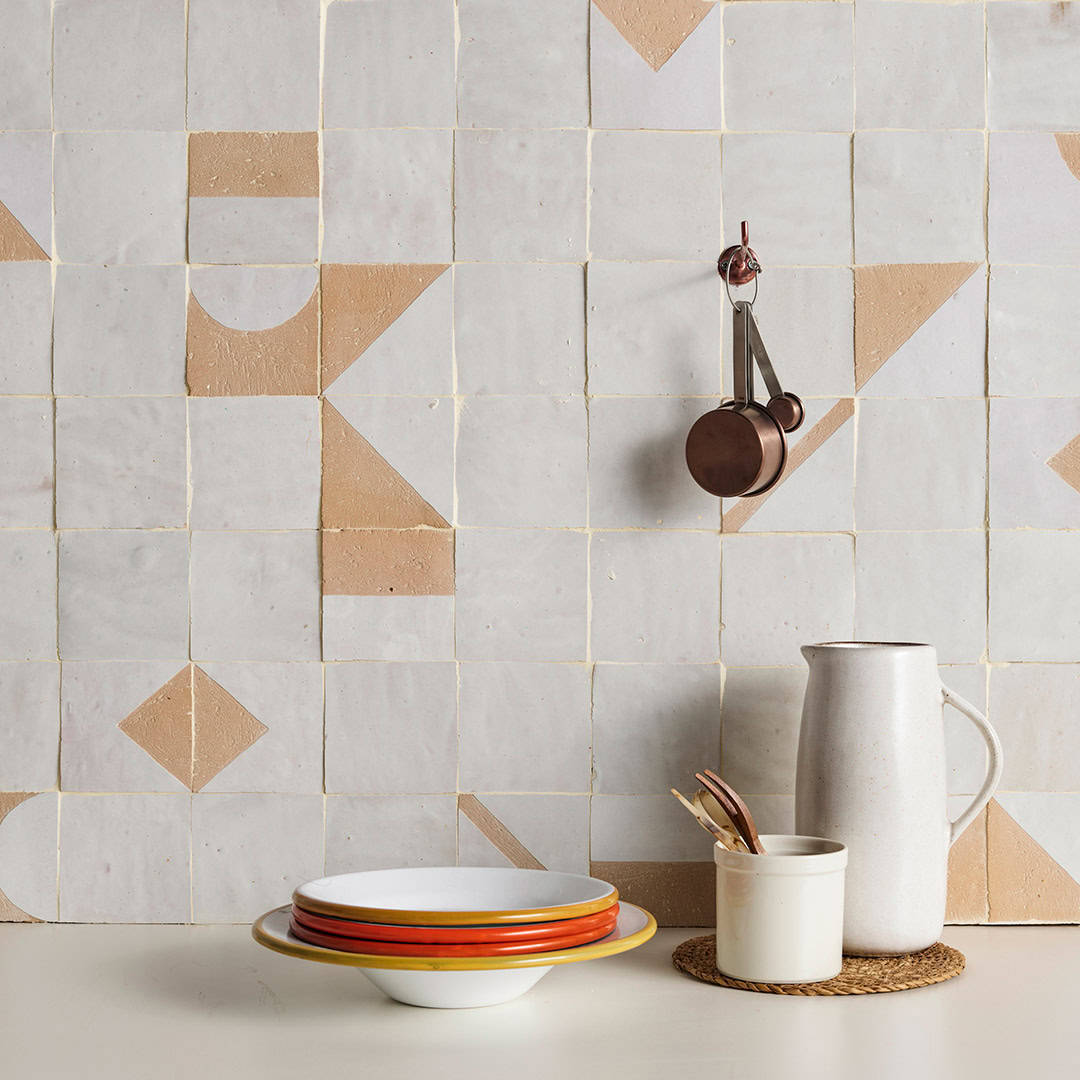 Minimalist kitchen setup with colorful bowls, a ceramic jug, and measuring spoons against a geometric tiled wall in soft pastel shades.