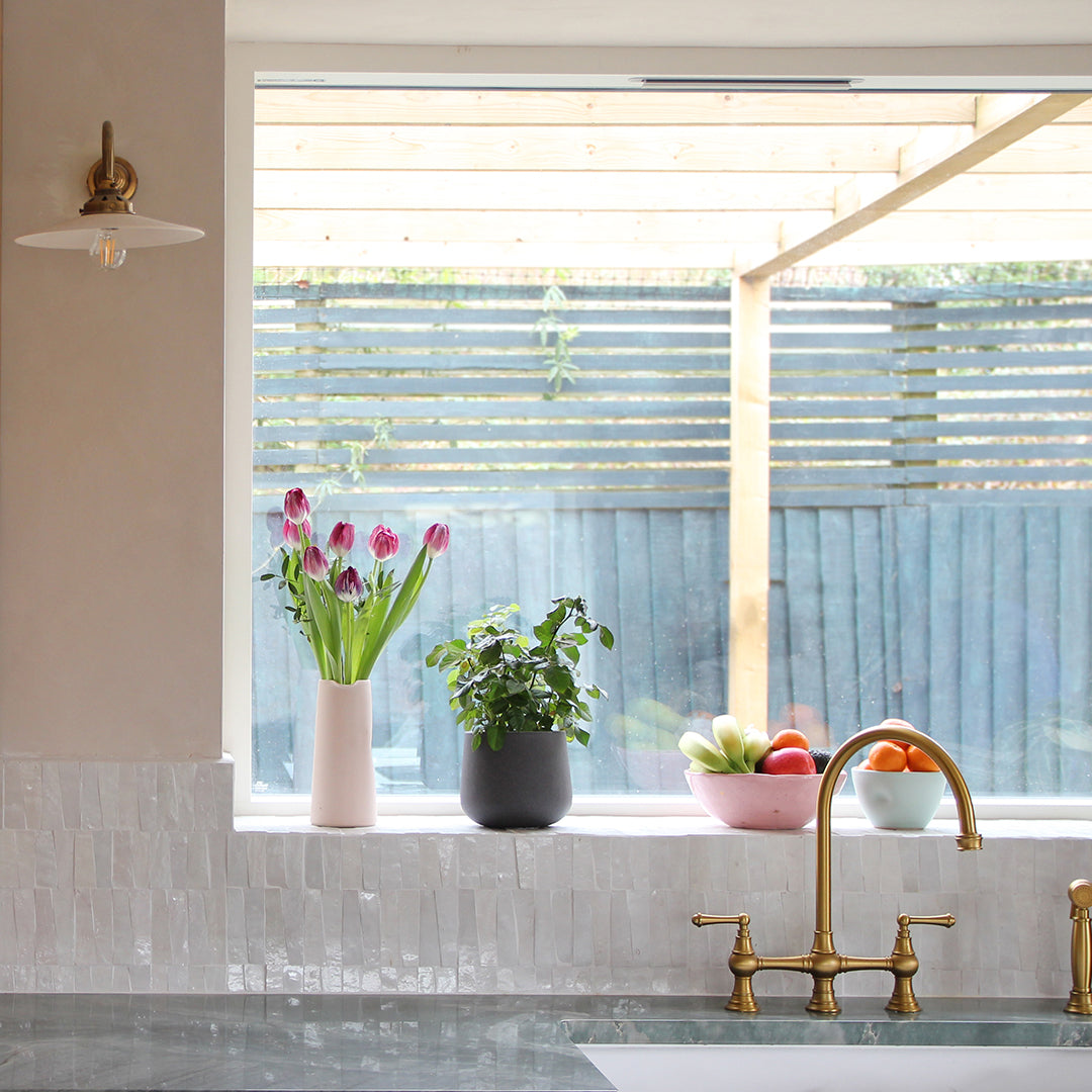 Kitchen with a window sill featuring flowers and plants, and a sink with a gold faucet.
