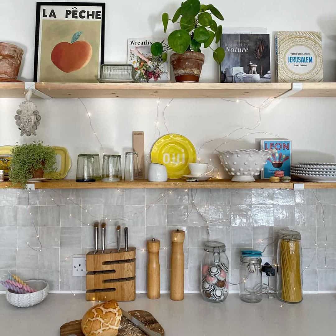 A neatly arranged kitchen with two wooden shelves on a white tiled wall. 