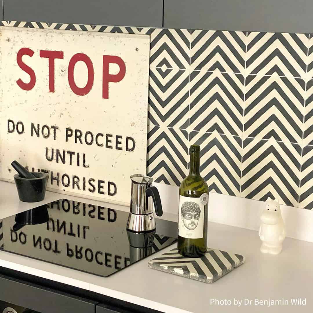 Square ceramic tile with bold chevron pattern of alternating dark gray textured and smooth off-white stripes, forming inverted V-shapes for modern geometric.